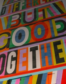 Closeup vertical view of a brick mural with colored letters scattered throughout.