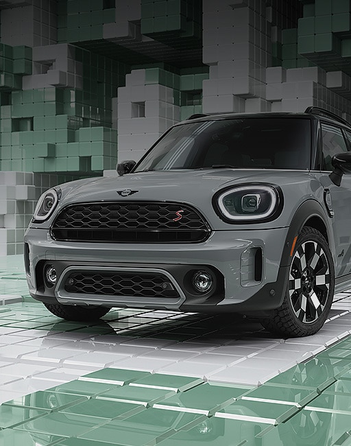 Three-quarters front view of a MINI Countryman Untamed Edition in Momentum Grey, parked in a CGI world made up of light green and white 3D, Tetris-like boxes.