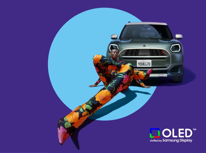 Front view of a 2025 MINI Countryman S parked on a blank surface with shadows underneath it, enclosed in a light blue circle, along with a fisheye view of a woman in floral clothing sitting in front of it and a logo reading “OLED vivified by Samsung Display” in the bottom right corner