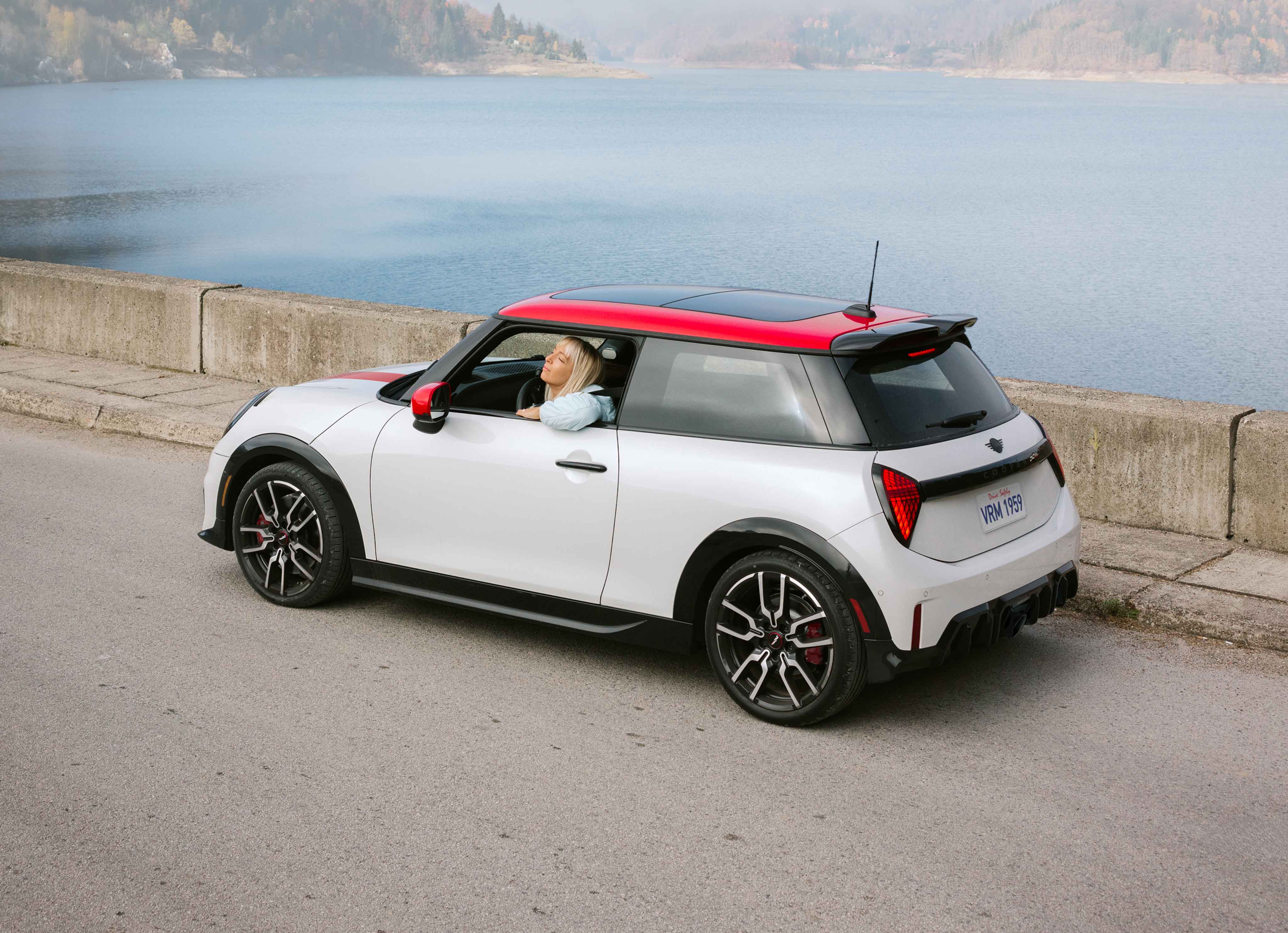 A woman looking out the window of her parked MINI JCW 2 Door in front of a lake.