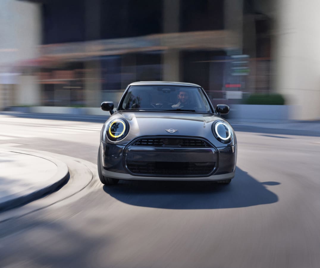 Front-view of a MINI Cooper 2 Door rounding a bend in a city environment.
