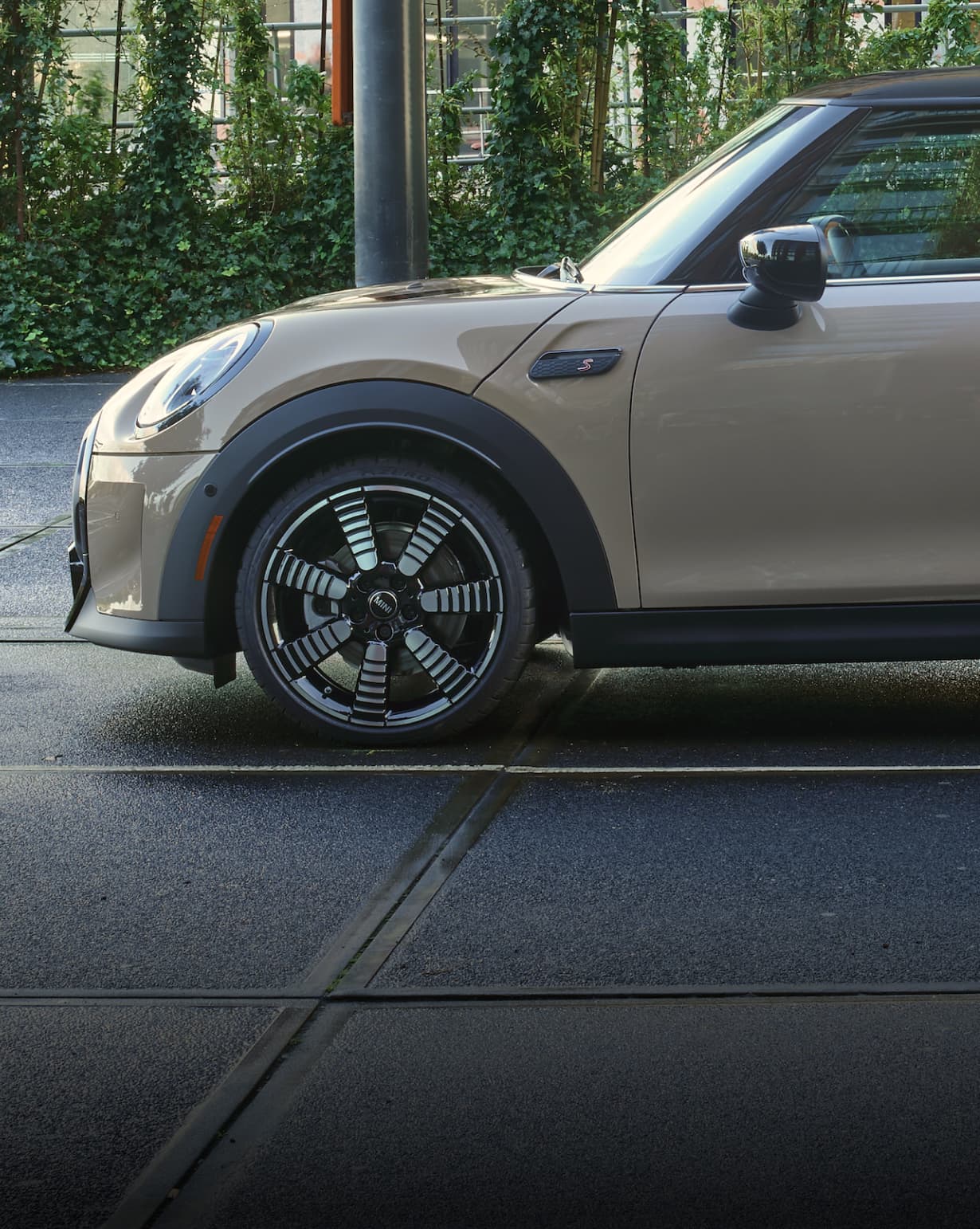 Side view of a grey MINI Hardtop 2 Door’s front-left wheel on a street surface with trees in the background.