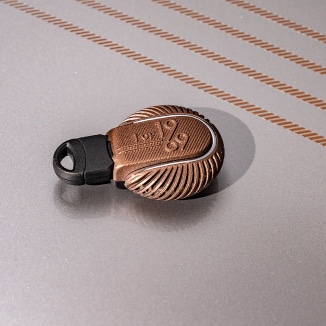 Closeup view of the MINI Cooper S Clubman ALL4 Final Edition’s customized key cover accessory sitting on top of a Melting Silver III surface with commemorative bonnet stripes nearby.
